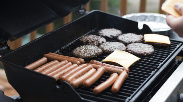 person standing in front grill grilling sausage